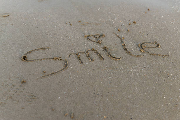On the sand of the beach someone has written a smile message with a small emoticon, no one can be seen, with copy space